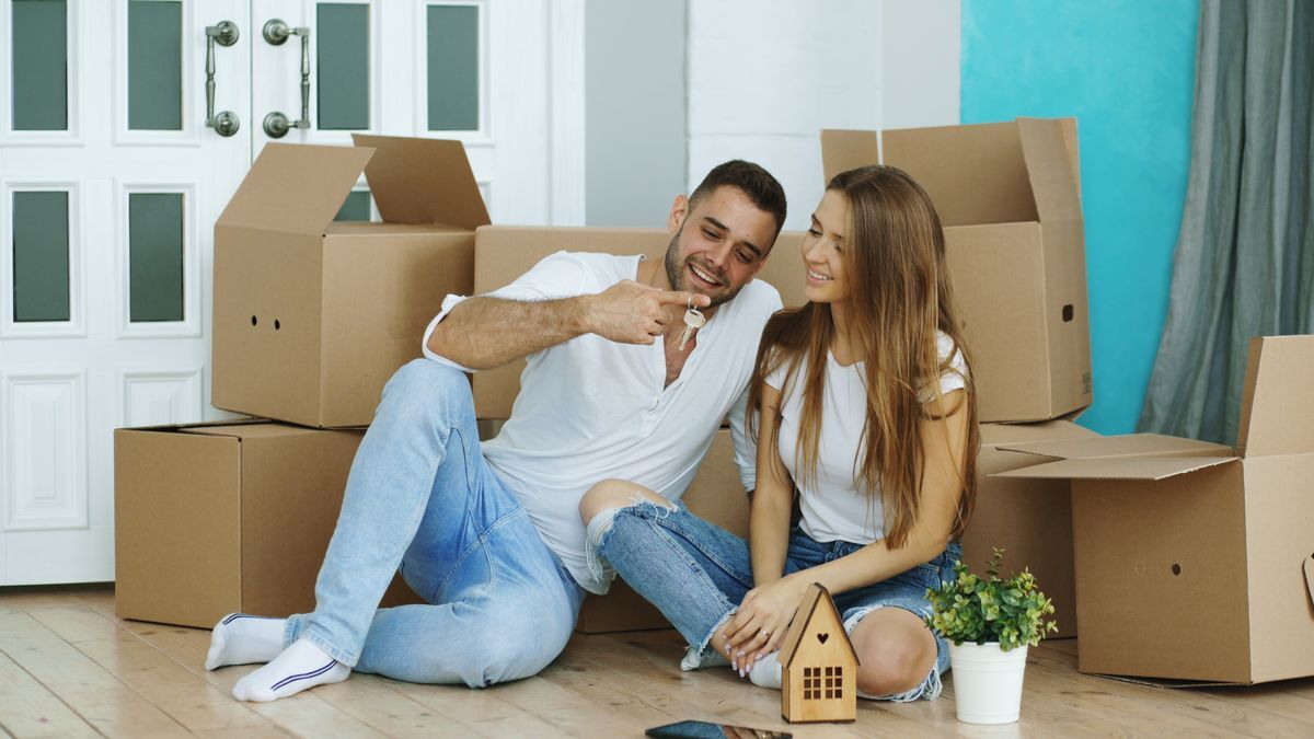 Pareja joven con las llaves de su piso de alquiler rodeada de cajas de mudanza