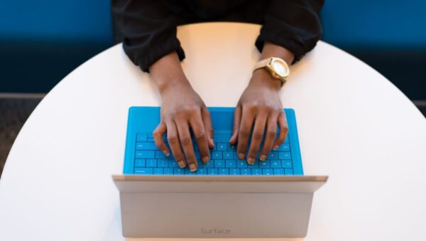 Persona escribiendo en el teclado de un portátil sobre una mesa de madera